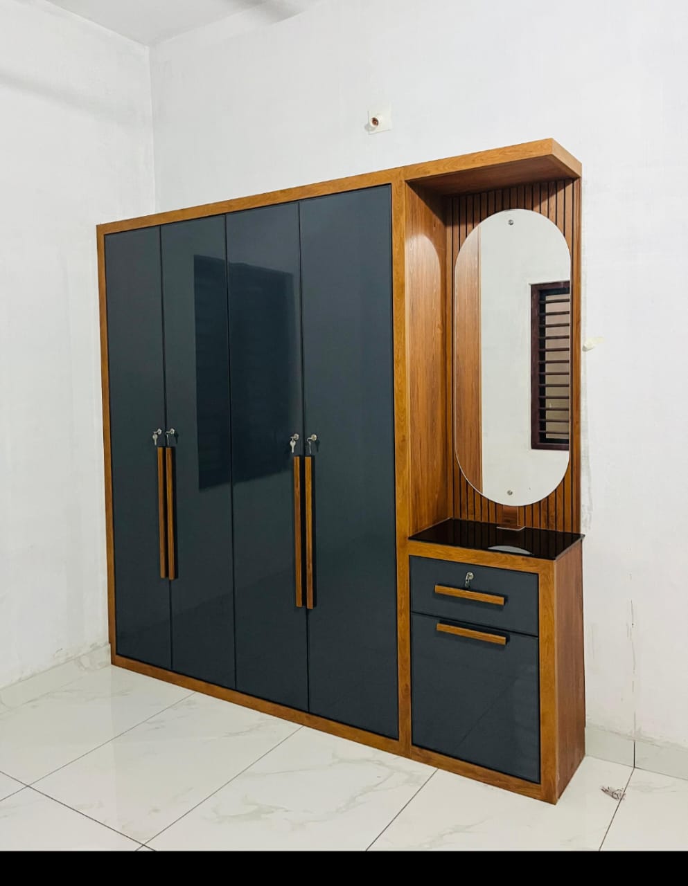 "Modern wooden wardrobe with matte black doors and an attached dressing unit featuring an oval mirror and storage drawers."